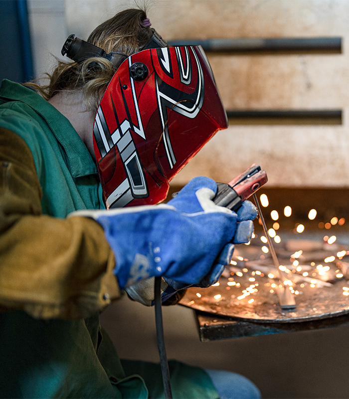 A Welding student welds a piece of metal.